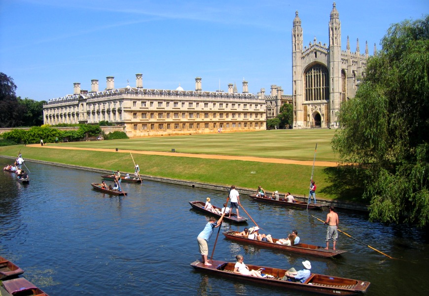 A photo of the University of Cambridge, with many people boating down the Cambridge River nearby.