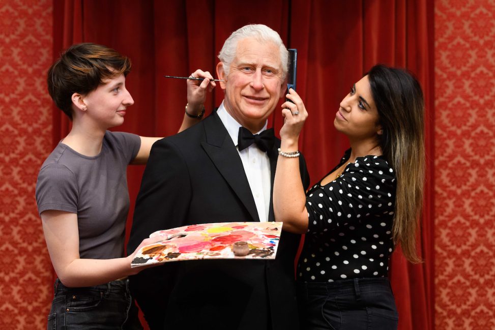 Two people standing with a wax sculpture of King Charles at Madame Tussauds.